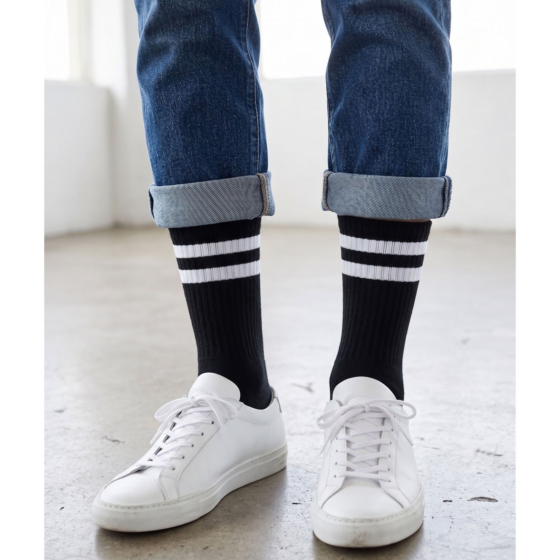 Black sport crew socks with white stripes worn with white trainers and rolled jeans
