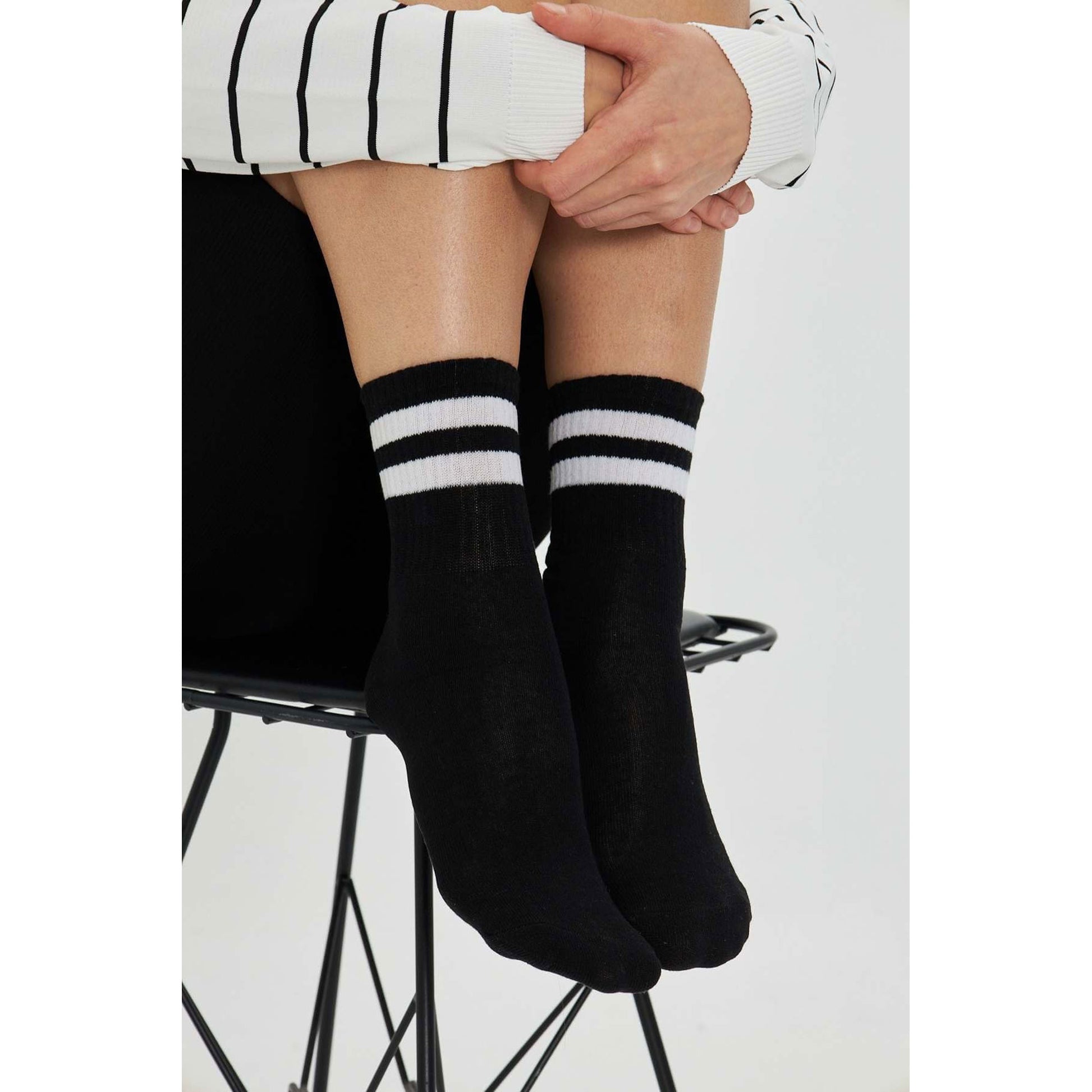 Black sport crew socks with white stripes worn, seated on a stool