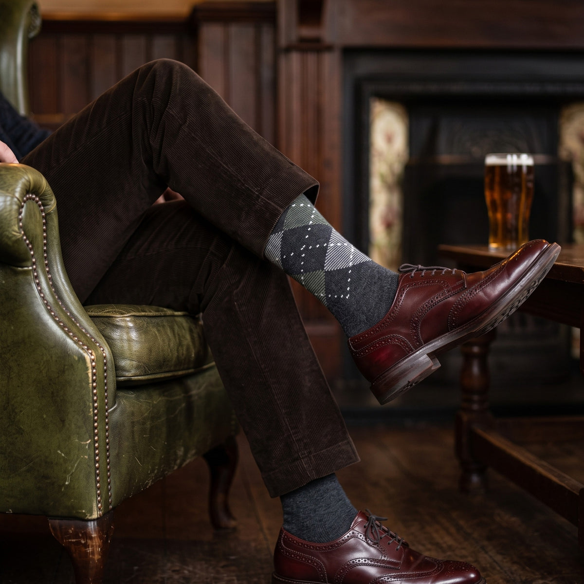 Man in a pub leather armchair wearing charcoal argyle lambswool socks with corduroy trousers and burgundy brogues