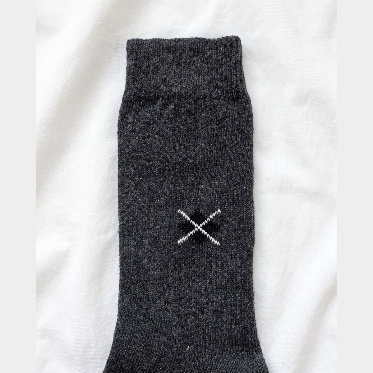 Close-up of charcoal lambswool sock showing the embroidered black diamond with white cross-stitch and ribbed cuff