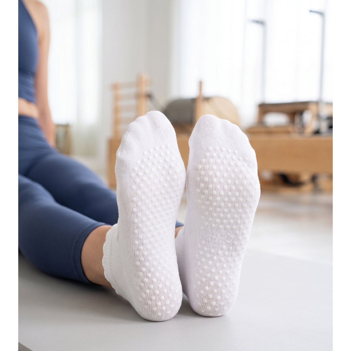 Model seated on a pilates mat showing white grip sock soles with grip dots