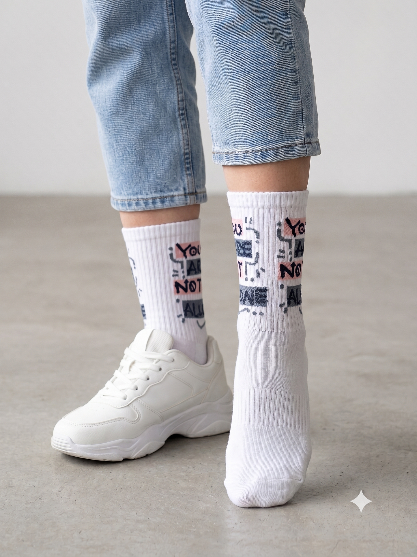 Model wearing white You Are Not Alone slogan grip socks with white trainers and jeans