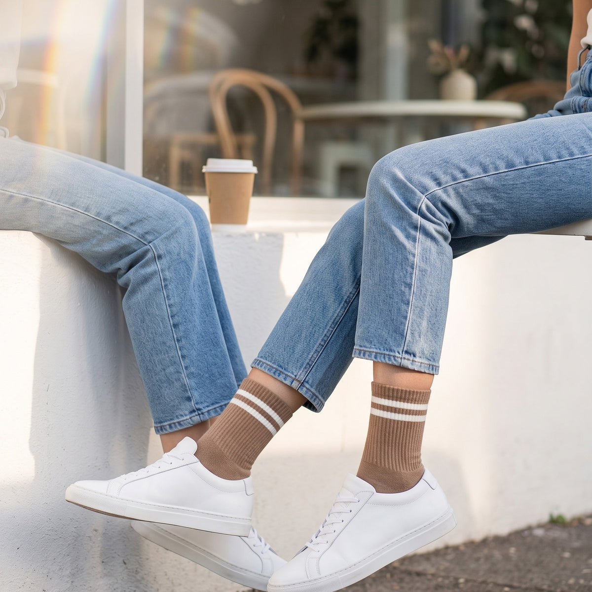 Woman outside a café wearing brown two-stripe tennis socks with light-wash jeans and white sneakers
