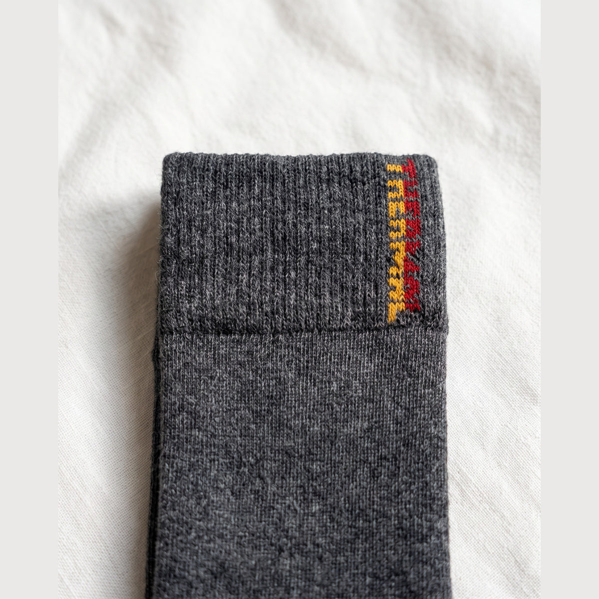 Close-up of charcoal Thermo sock showing the ribbed cuff and knitted yellow and red THERMO lettering